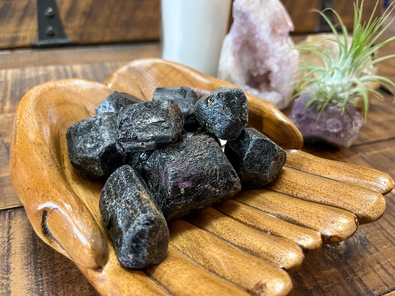May include: A collection of black tourmaline crystals in a wooden hand-shaped bowl. The crystals are rough and have a natural, unpolished look.