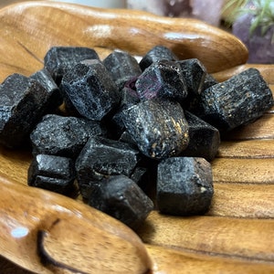 May include: A collection of black tourmaline crystals in a wooden bowl. The crystals are rough and have a natural, unpolished look.