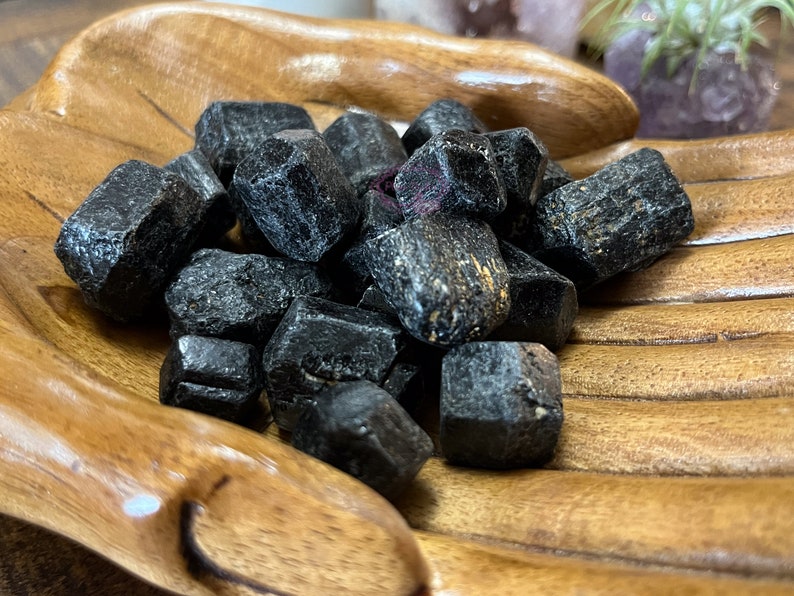 May include: A collection of black tourmaline crystals in a wooden bowl. The crystals are rough and have a natural, unpolished look.