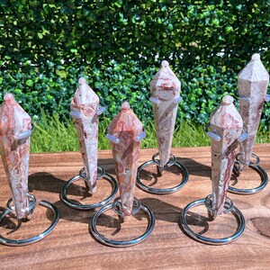 May include: Six polished, multi-faceted stone points with swirling patterns of red, white, and tan. Each crystal point is held upright by a silver-toned metal ring stand, creating a vertical display of these natural mineral specimens.