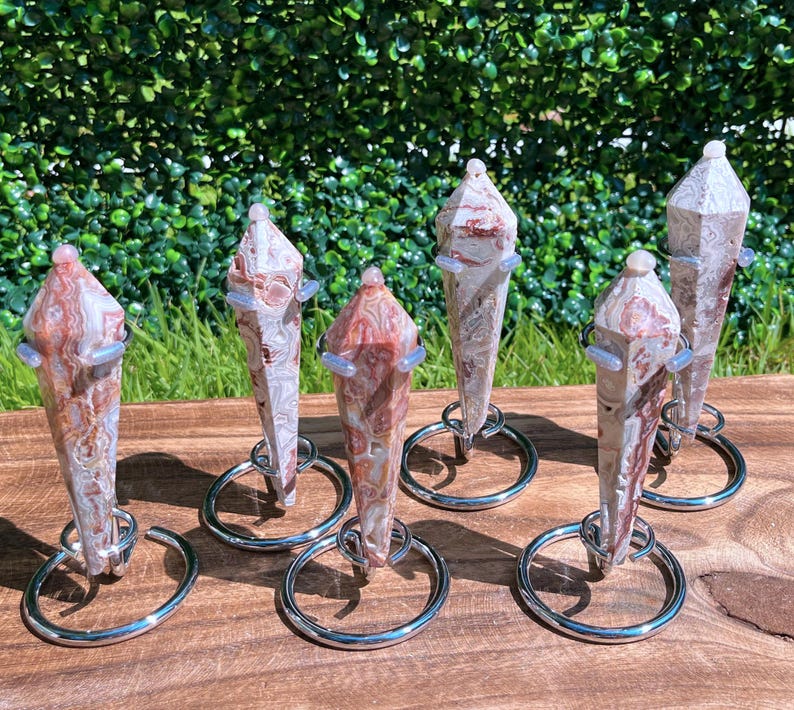 May include: Six polished, multi-faceted stone points with swirling patterns of red, white, and tan. Each crystal point is held upright by a silver-toned metal ring stand, creating a vertical display of these natural mineral specimens.
