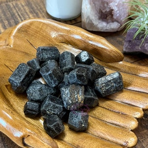May include: A wooden hand-shaped bowl filled with black tourmaline crystals. The crystals are rough and have a natural, unpolished look.