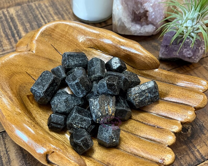 May include: A wooden hand-shaped bowl filled with black tourmaline crystals. The crystals are rough and have a natural, unpolished look.