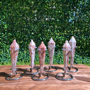 May include: Six polished, multi-faceted stone points with swirling patterns of cream, tan, and reddish-brown hues. Each stone is secured in a circular, silver-toned metal wire stand that holds the crystal upright in a vertical position.
