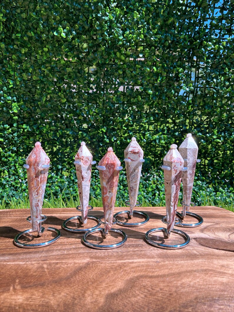 May include: Six polished, multi-faceted stone points with swirling patterns of cream, tan, and reddish-brown hues. Each stone is secured in a circular, silver-toned metal wire stand that holds the crystal upright in a vertical position.
