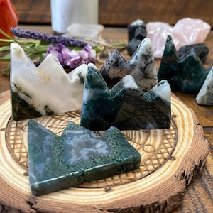 May include: A set of six green, white, and black agate mountain carvings. The carvings are arranged on a wooden base with a circular design.