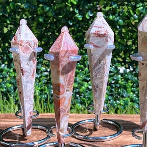 May include: Six polished stone points with intricate swirling patterns in shades of cream, tan, and reddish-brown. Each faceted crystal tower is held upright by a silver-toned metal stand featuring a circular base and small support arms.