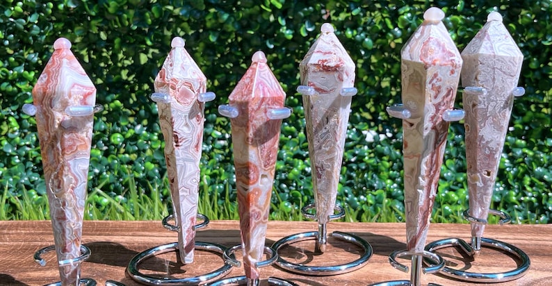 May include: Six polished stone points with intricate swirling patterns in shades of cream, tan, and reddish-brown. Each faceted crystal tower is held upright by a silver-toned metal stand featuring a circular base and small support arms.