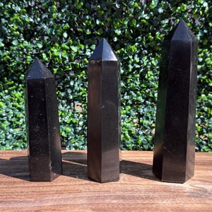 May include: Three polished black stone towers with hexagonal bases and pointed tops arranged in a row. The stones have a smooth, dark surface with subtle reflective qualities, standing upright in varying heights from shortest to tallest.