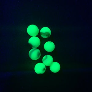 May include: A group of eight green marbles with white swirls, glowing under a blacklight.