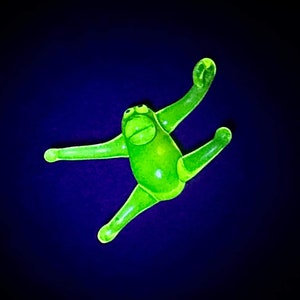May include: A bright green, rubber, toy monkey with a playful expression. The monkey is in a jumping pose with its arms and legs outstretched.