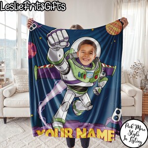 Puede incluir: Una manta personalizada con un dise&ntilde;o de dibujos animados de Buzz Lightyear y la cara de un ni&ntilde;o. La manta tiene un fondo azul oscuro con planetas y estrellas. El texto "YOUR NAME" est&aacute; en la parte inferior en amarillo.