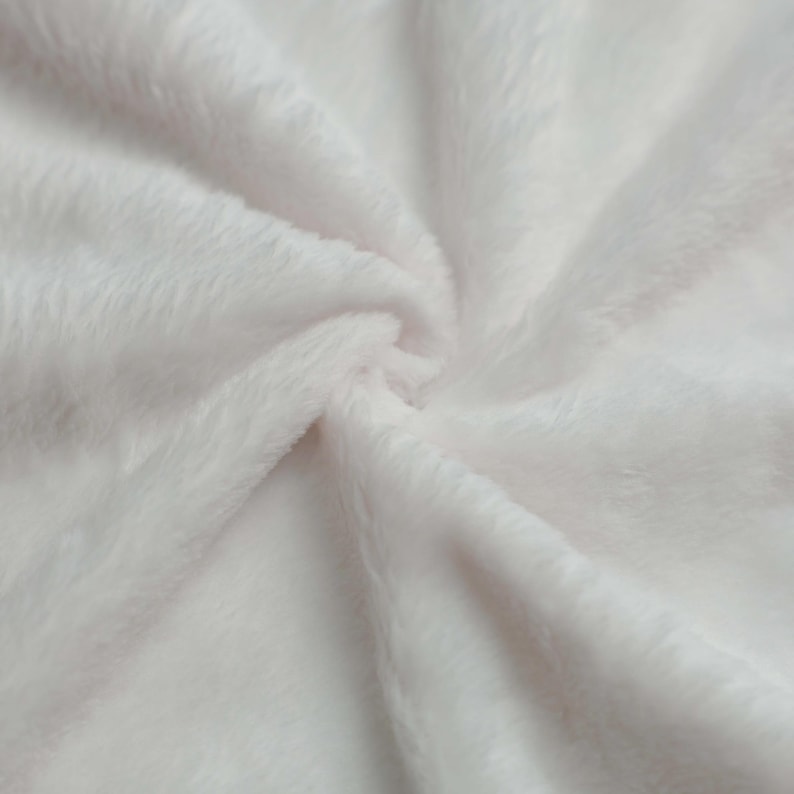 Puede incluir: Primer plano de una tela suave, blanca y esponjosa. El material tiene una textura afelpada con fibras visibles y un ligero brillo. La tela est&aacute; dispuesta en pliegues suaves, creando una sensaci&oacute;n de profundidad y suavidad. Ideal para mantas, mantas o ropa.
