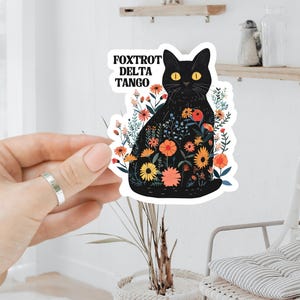 May include: Black cat sticker with a floral design and the text "FOXTROT DELTA TANGO".