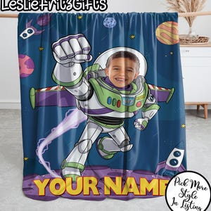 Puede incluir: Una manta personalizada con un dise&ntilde;o de dibujos animados de Buzz Lightyear, que incorpora la cara de un ni&ntilde;o. La manta tiene un fondo azul espacial con planetas, estrellas y un cohete. Las palabras "YOUR NAME" se muestran en amarillo.