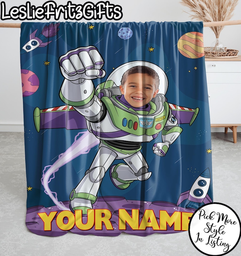 Puede incluir: Una manta personalizada con un dise&ntilde;o de dibujos animados de Buzz Lightyear, que incorpora la cara de un ni&ntilde;o. La manta tiene un fondo azul espacial con planetas, estrellas y un cohete. Las palabras "YOUR NAME" se muestran en amarillo.