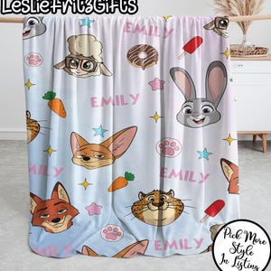 Puede incluir: Una manta azul claro con personajes de dibujos animados, estrellas, huellas de patas y el nombre "Emily" en rosa. La manta presenta un zorro, un conejo, una oveja y otros personajes.