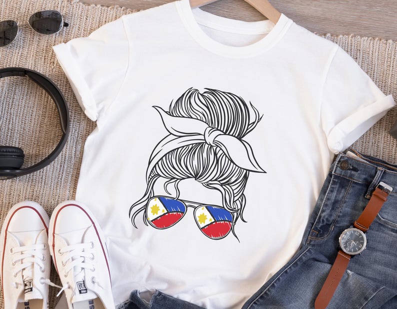 May include: White t-shirt featuring a black and white illustration of a woman's updo hairstyle with a bandana. The woman is wearing sunglasses with the Philippine flag design. The shirt is paired with blue jeans and white sneakers.