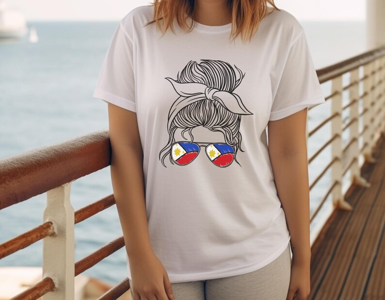 May include: White t-shirt featuring a graphic of a woman's hair styled in a bun with a headband. The sunglasses have the colors of the Philippine flag. The background shows a body of water and a wooden deck.