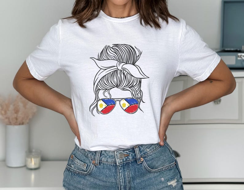 May include: White t-shirt featuring a black and white graphic of a woman's updo hairstyle with sunglasses. The sunglasses have the colors of the Philippine flag. The shirt is a crew neck and is made of a soft material.