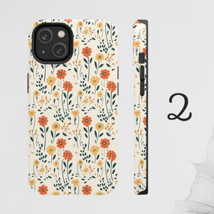 May include: A white phone case with a floral pattern featuring orange, yellow, and green flowers. The case has a black camera cutout and a black side.
