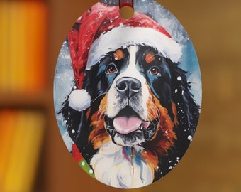 May include: Oval Christmas ornament featuring a Bernese Mountain Dog wearing a Santa hat. The ornament has a red ribbon for hanging. The dog's face is detailed with black, brown, and white fur, and a red tongue.