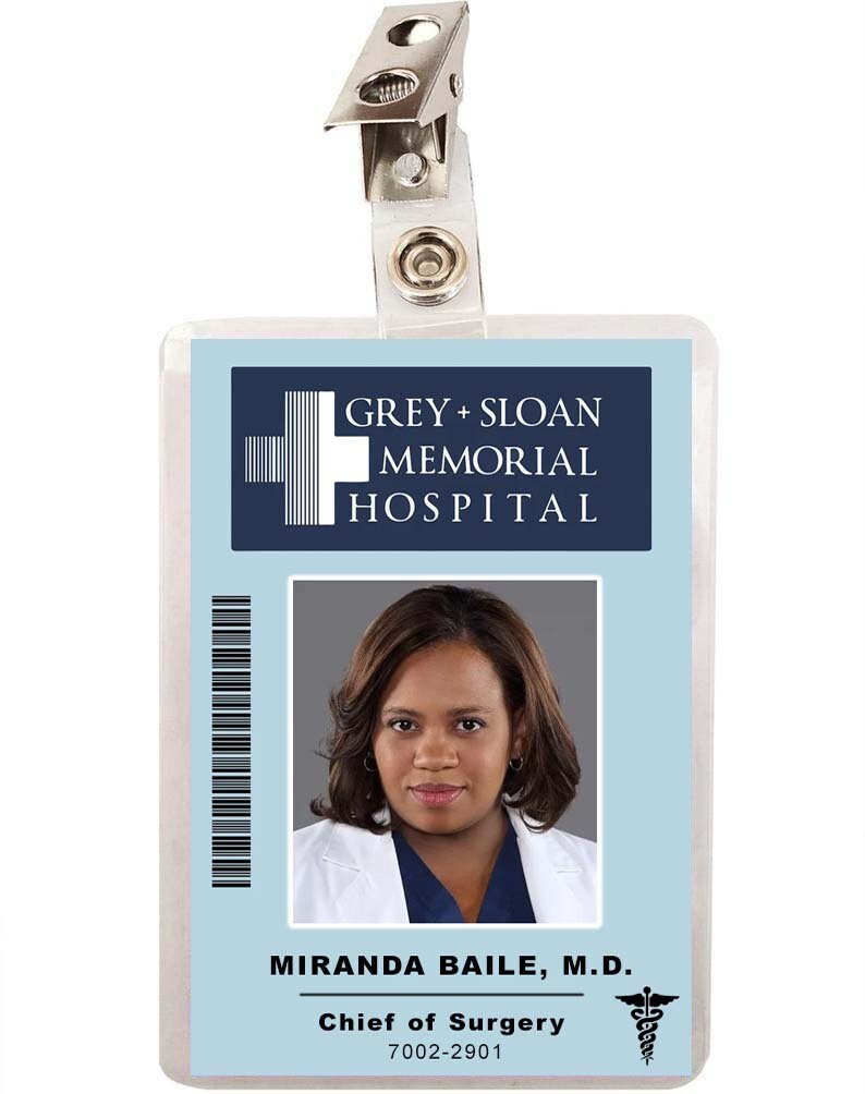 May include: A blue and white plastic ID badge with a photo of a woman with dark hair and a white lab coat. The badge reads "GREY + SLOAN MEMORIAL HOSPITAL" and "MIRANDA BAILE, M.D. Chief of Surgery 7002-2901".