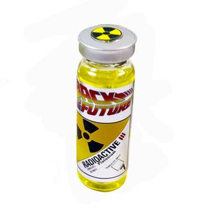 Puede incluir: Vial de vidrio con tapa plateada y líquido amarillo. La etiqueta dice "BACK TO THE FUTURE" con un símbolo radiactivo y la palabra "RADIOACTIVE". Accesorio de película.