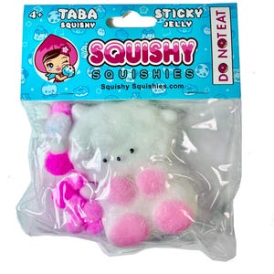 May include: A white plush toy with pink paw pads and a pink flower accessory is packaged in a clear plastic bag. The packaging features the text "Squishy Squishies" and "Sticky Jelly". The top of the package is blue with cartoon graphics.