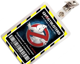 May include: A rectangular Ghostbusters ID badge with a clear plastic cover and metal clip. The badge features the Ghostbusters logo, text that reads "WE'RE READY TO BELIEVE YOU!", and a barcode. The background is black and blue with yellow and black borders.