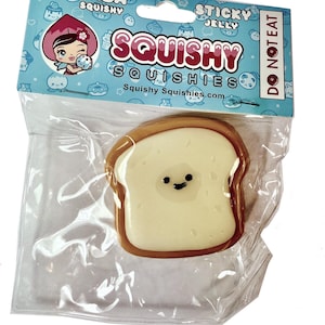 May include: A slice of bread-shaped squishy toy with a smiling face, packaged in clear plastic. The packaging features the words "Squishy Squishies" and "Sticky Jelly". The background is light blue with cartoon illustrations.