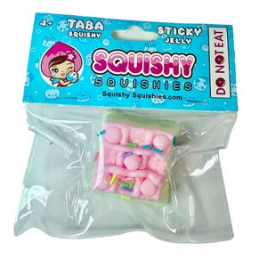 May include: A pink squishy toy shaped like a cake, packaged in a clear plastic bag. The packaging features the text "Squishy Squishies" and a cartoon character. The toy has pink frosting and colorful sprinkles. The packaging also says "Do Not Eat".