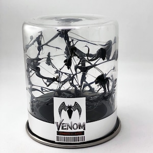 May include: A clear plastic container with a black base and a silver lid. Inside the container is a black, gooey substance that resembles a symbiote. The container has a label that reads "Venom Symbiote V1 -  E0170".