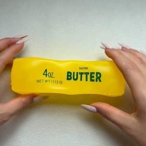 May include: A bright yellow rectangular stick of salted butter in a plastic wrapper. The text on the front reads 4 oz. NET WT. (113 g) and SALTED BUTTER in bold green lettering. The packaging is smooth and slightly translucent with rounded edges.