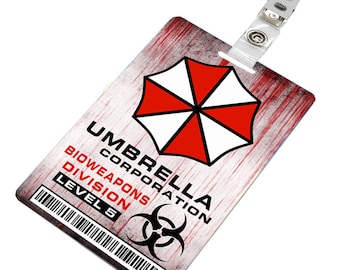 Könnte beinhalten: Ein rotes und weißes Schirmlogo mit dem Text "Umbrella Corporation" und "Bioweapons Division Level 5" auf einem rot-weißen Grunge-Hintergrund. Das Logo befindet sich auf einer weißen Plastikkarte mit einem durchsichtigen Plastikband und einem Metallclip.