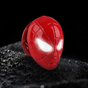 May include: A red plastic toy mask of Spider-Man with white glowing eyes. The mask is detailed with the iconic web pattern.