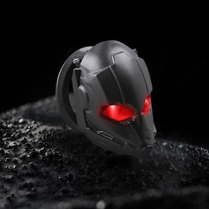 May include: A black plastic helmet with red glowing eyes. The helmet has a textured surface and a rounded shape.
