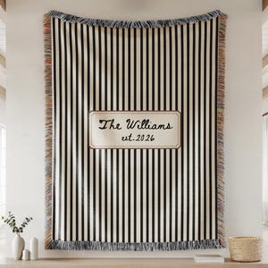 May include: A woven throw blanket featuring vertical black and cream stripes with fringed edges. A central rectangular cream-coloured patch displays the black text The Williams and est. 2026 in a script and sans-serif font combination.