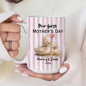 May include: White ceramic mug with pink vertical stripes, featuring the text "Our first Mother's Day" and a watercolor illustration of two ducks. The mug also includes the text "Mommy & Jacob -2026-".
