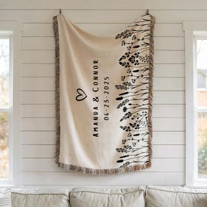 May include: Cream-colored woven throw blanket with black floral and foliage design along the right edge. The blanket features the names "Amanda & Connor" and the date "06-23-2025" in black text, along with a heart symbol.