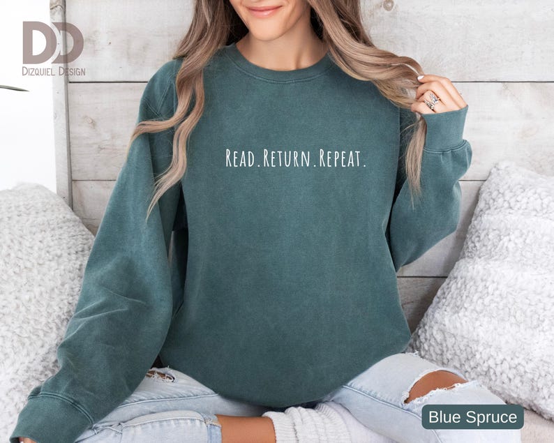 May include: A teal-colored sweatshirt with the text "READ. RETURN. REPEAT." in white lettering. The sweatshirt is a solid color and has long sleeves. The bottom right corner of the image has the text "Blue Spruce".