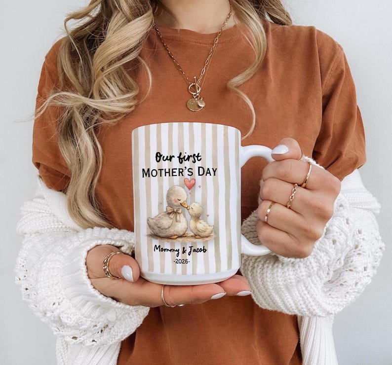 May include: White ceramic mug with vertical beige stripes. The mug features the text "Our first MOTHER'S DAY" and a watercolor illustration of two ducks. Below the illustration is the text "Mommy & Jacob -2026".
