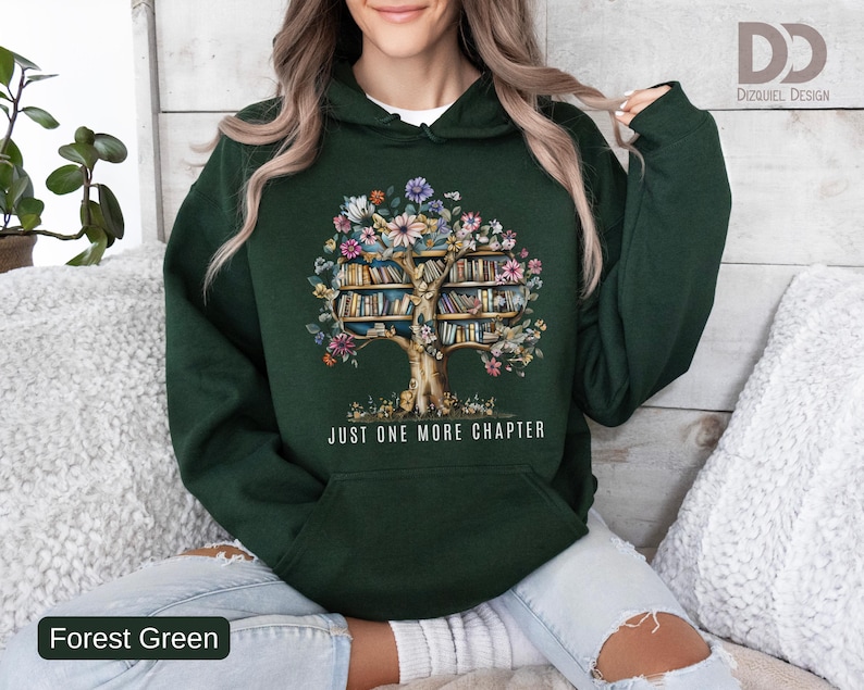 Puede incluir: Sudadera con capucha verde bosque con un dise&ntilde;o de &aacute;rbol. El &aacute;rbol presenta un tronco y ramas llenas de libros y flores coloridas. El texto "JUST ONE MORE CHAPTER" est&aacute; impreso debajo del &aacute;rbol.