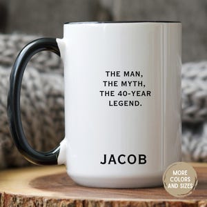 May include: White ceramic mug with a black handle and rim. The mug features the text "THE MAN, THE MYTH, THE 40-YEAR LEGEND." and the name "JACOB" in black. A small button on the bottom right says "MORE COLORS AND SIZES."