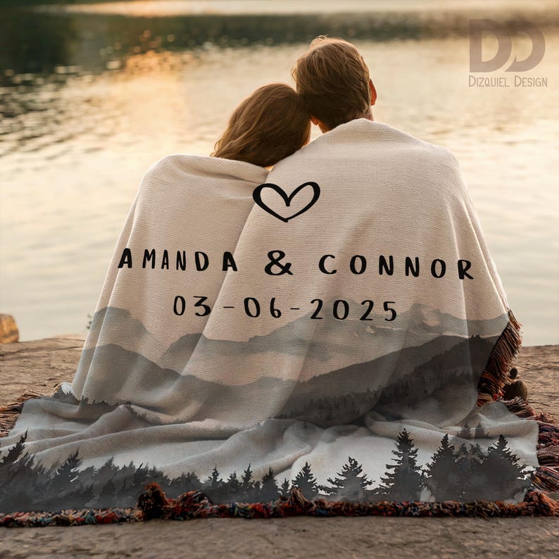 May include: A personalized blanket with a mountain landscape design, draped over a couple. The blanket features the names "AMANDA & CONNOR" and the date "03-06-2025" with a heart symbol. The blanket has a fringed edge.