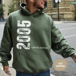 Pu&ograve; includere: Felpa con cappuccio verde militare con una grande grafica bianca "2005" e testo "LIMITED EDITION". Presenta una tasca frontale e un cappuccio. La felpa &egrave; di colore uniforme e sembra essere realizzata in un materiale morbido.