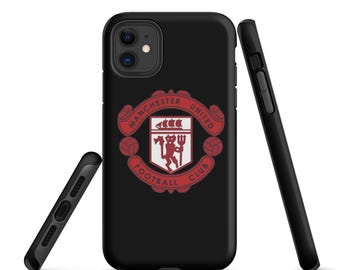 May include: Black iPhone case featuring the Manchester United Football Club logo in red and white. The logo includes a ship, a devil holding a trident, and the words "Manchester United Football Club". Two additional black phone cases are also visible.