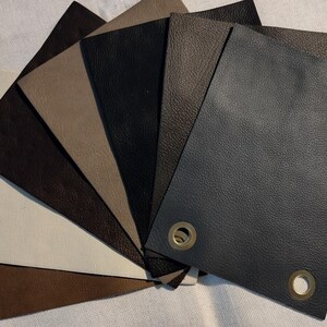 May include: A fan of leather swatches in various shades of brown, beige, and black. The samples are arranged to display the different textures and colors. Some swatches have brass eyelets.