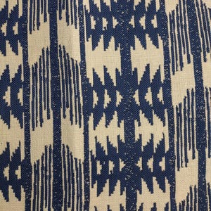 May include: Close-up of a fabric with a repeating geometric pattern. The design features a combination of navy blue and off-white colors. The pattern includes vertical lines and diamond-like shapes, creating a textured appearance.