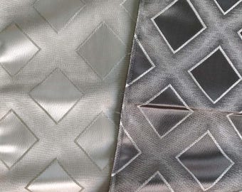 Op de afbeelding: Een stofstaal met een herhalend geometrisch ruitpatroon. De linkerkant vertoont een lichte zilvergrijze tint, terwijl de rechterkant overgaat in een donkerder antracietgrijs. De ruiten zijn omlijnd met dunne, scherpe lijnen.